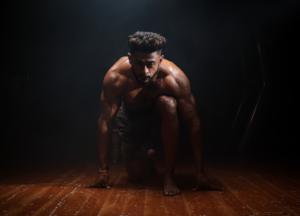 Hardcore fitness model crouching on wooden floor with intense lighting representing testosterone support and performance optimisation