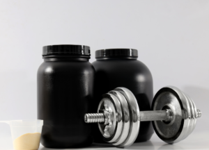 Pre-workout powder scoops, supplement capsules, and tablets beside a shaker bottle, representing stimulant supplements, sports nutrition, and workout performance products.