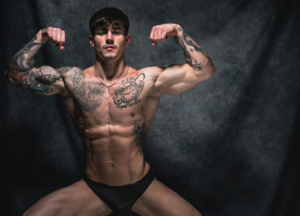 Lean muscular bodybuilder performing a front double biceps pose, showcasing developed chest, shoulders, arms, and abdominal definition during a bodybuilding physique assessment.