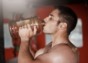 Athlete drinking water from a large bottle during a workout, highlighting hydration, recovery, and sports performance support.
