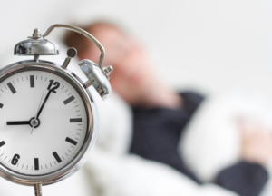 Sleep and Muscle Recovery: Alarm clock beside a sleeping person illustrating consistent sleep schedule, healthy sleep duration, circadian rhythm and improved overnight recovery